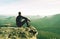 Man sits on edge of cliff against background of mist