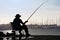 A man sits with a fishing rod in his hand at a harbor basin in Spain.