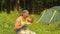 A man sits near a tent in the forest and eats fruit salad.