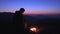 A man sits at night by a fire in the mountains. A tourist admires the landscape and looks at the burning fire