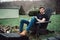 Man sits outdoors on a wooden chair on the backyard of his house at rural area.