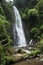 A man sits on a rock beside Catarata Zamora waterfall in Los Chorros park, Costa Rica.