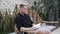 Man sits on wicker bench and reads book, tropical greenery on background