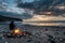 Man Sitting on Beach Next to Fire