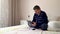 A man is sitting on the bed with a tablet and a phone. Real people, homemade footage