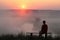 Man sitting on bench and watching misty sunrise