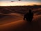 Man sitting on a dune in the desert while watching the sunset.