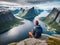 a man is sitting on the edge of a cliff and looking at the view of the mountains