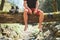 Man sitting on the fallen tree log over the mountain forest stream while he waiting for socks laundry drying and trekking boots.