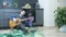Man sitting on the floor at kitchen and tuning guitar. Young male singer playing guitar and learning new chords. Online guitar les