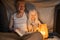 Man sitting with his little albino daughter and reading book by the light of the lamp