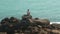 Man sitting on a huge boulder on a beach and looking at the sea