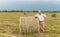 A man sitting on a large armful of straw in an empty field