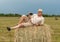 A man sitting on a large armful of straw in an empty field