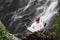 Man sitting in meditation yoga on rock at waterfall in tropical