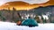 A man sitting near tent on snow pours tea from thermos