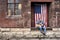 Man sitting on old factory loading dock wearing jeans with acoustic guitar and American flag