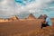 Man sitting on the sandy desert dunes posing in front of the great pyramids of giza. Traveling egypt in winter time, tourists