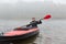 Man sitting smiling in kayak and holding paddle in hands, sportsman wearing black jacket rowing boat in foggy morning, water sport