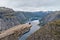 Man sitting on Trolltunga rock and looking at Norwegian mountain landscape