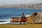 Man sitting on wood bench looking at panorama of idyllic and amazing seaside landscape of jagged shore, rocks, hillside buildings