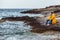 man sitting in yellow raincoat at rocky beach looking at stormy weather