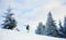 Man skier in goggles carrying skis and walking down along fir trees forest in snow-capped mountains. Side low angle view