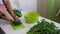 A man slices parsley with a knife on a chopping Board. Next to the table there is a lot of parsley and beet tops