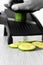 Man slicing cucumber with a mandoline on a grey wood kitchen worktop