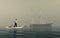 Man on a small boat looking at a near old ship .