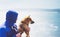 Man with small golden japanese shiba inu dog sitting togetherness on a mountain and looking at blue sea horizon, friends on relax