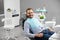 Man is smiling to the camera while sitting in a dental chair in dentistry being happy and satisfied with his treatment.