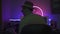 Man smoke hookah in dark room at work place with neon light. Rear view of male silhouette sitting at home desk. Work