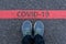 Man in sneakers standing next to a red line with text COVID-19