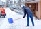 Man with snow shovel cleans sidewalks in winter during snowfall. Winter time in Europe. Young man in warm winter clothes