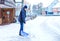 Man with snow shovel cleans sidewalks in winter during snowfall. Winter time in Europe. Young man in warm winter clothes