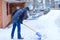 Man with snow shovel cleans sidewalks in winter during snowfall. Winter time in Europe. Young man in warm winter clothes