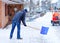 Man with snow shovel cleans sidewalks in winter during snowfall. Winter time in Europe. Young man in warm winter clothes