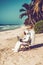 Man in space suit sitting on chair on beach using laptop. Generative AI