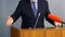 Man speaks in front of microphones, gesturing and standing behind a podium or pulpit. Lawyer, politician, businessman or teacher.