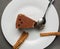 A man with a spoon breaks off a piece of chocolate cake on a white dish. cinnamon rolls nearby.