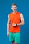 Man with sport smartwatch on violet wall. Sportsman in orange vest and blue shorts. Fashion accessory for training and