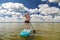 A man in sports shorts with a paddle stands on a SUP board in the lake against the background of white clouds on a clear