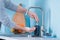 A man squeezes soap on his hand in the kitchen against the background of blue walls