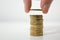 Man stacking Euro coins on a white desk, holding a coin between finger and thumb. Close up.