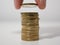 Man stacking Euro coins on a white desk, holding a coin between finger and thumb. Close up.