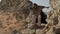 A man with a staff in his hand and the clothes of a shaman stands on a rock among the sands of the desert and dances