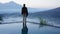 Man standing alone from behind on the edge of the pool at sunrise with water reflection and blue mount Batur view background.