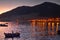 Man standing in boat rowing at late evening with coastal lights and mountains in background