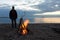 Man standing by the bonfire near the river at sunset